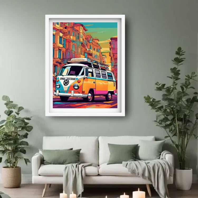 A framed pop-art print of a classic Volkswagen camper van driving through a colorful city street, displayed on a light gray wall above a white sofa with green pillows and plants in a modern living room setting.