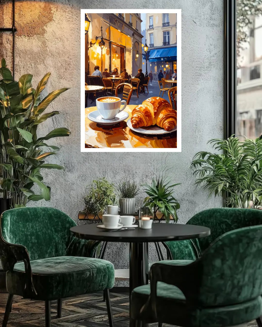 A framed wall art print depicting a cozy Parisian cafe scene with a croissant and coffee cup, displayed on a textured gray wall above a round black table with green velvet chairs in a styled interior.