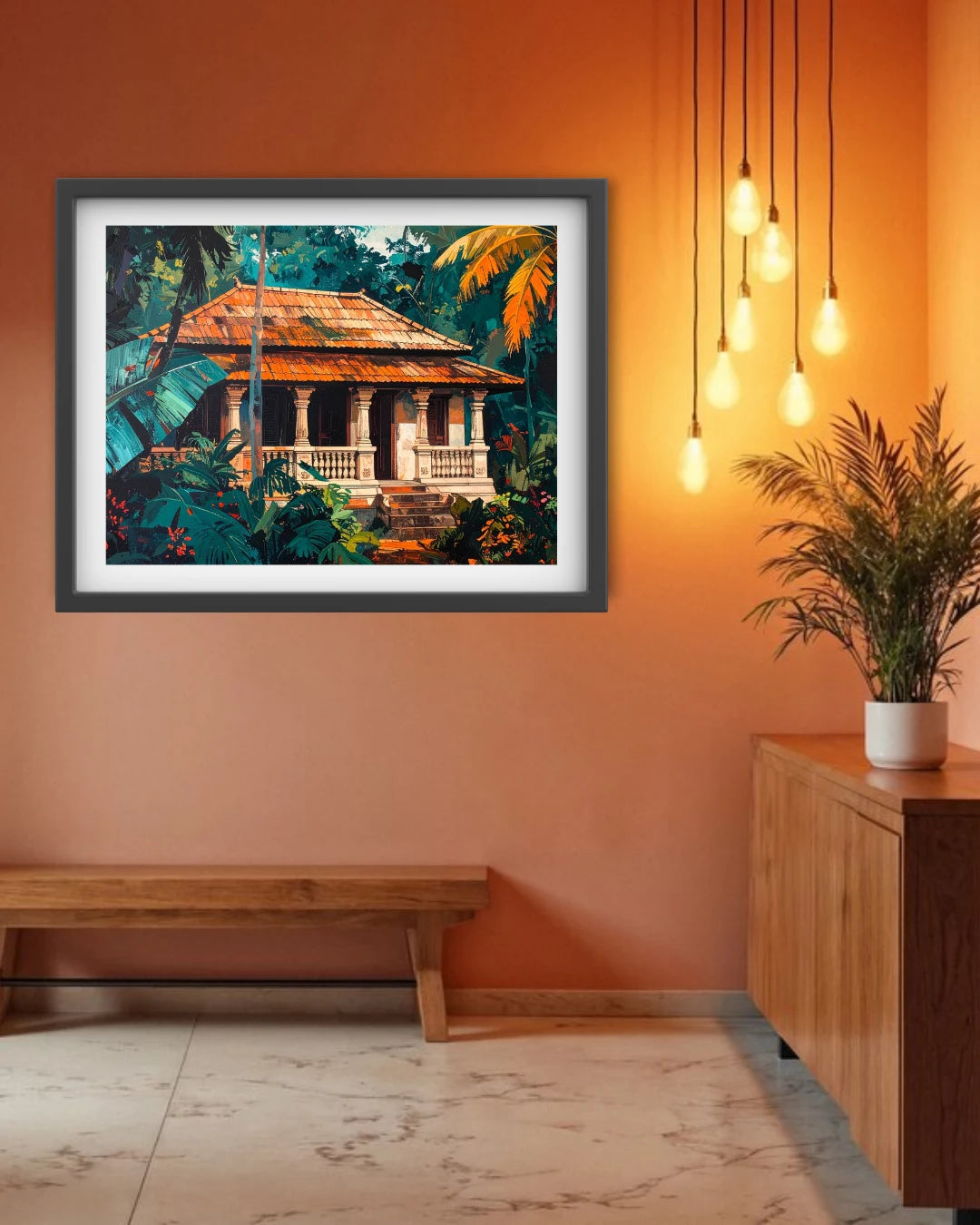 A framed art print depicting a tropical house surrounded by lush green foliage, displayed on a terracotta-colored wall in a modern room setting with a wooden bench, cabinet, and hanging pendant lights.