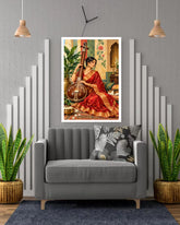 A framed art print depicting a woman in a red saree playing a stringed instrument, displayed on a gray wall above a modern gray sofa in a styled living room setting.