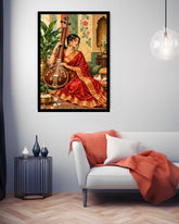 A framed art print depicting a woman in a red sari playing a stringed instrument, displayed on a light gray wall above a modern white sofa with a rust-orange throw blanket in a styled living room.