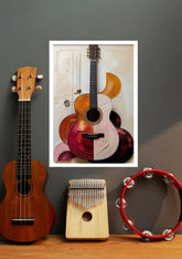 A framed art print featuring a stylized, colorful acoustic guitar illustration is displayed on a dark gray wall above a wooden surface. In the foreground, a brown wooden ukulele, a wooden kalimba, and a red tambourine are arranged as props.
