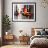 A framed abstract cityscape art print hangs on a light gray wall above a bed in a modern bedroom. The artwork features a vibrant, colorful urban street scene with tall buildings, yellow taxis, and reflections on wet pavement.