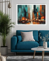 A framed abstract cityscape painting in teal, orange, black, and white hangs on a light gray wall above a blue sofa in a modern living room setting.