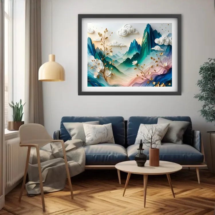 A framed abstract landscape art print hangs on a light gray wall above a blue sofa in a modern living room. The artwork features layered mountains in teal, blue, and pink tones with white clouds and golden branches.