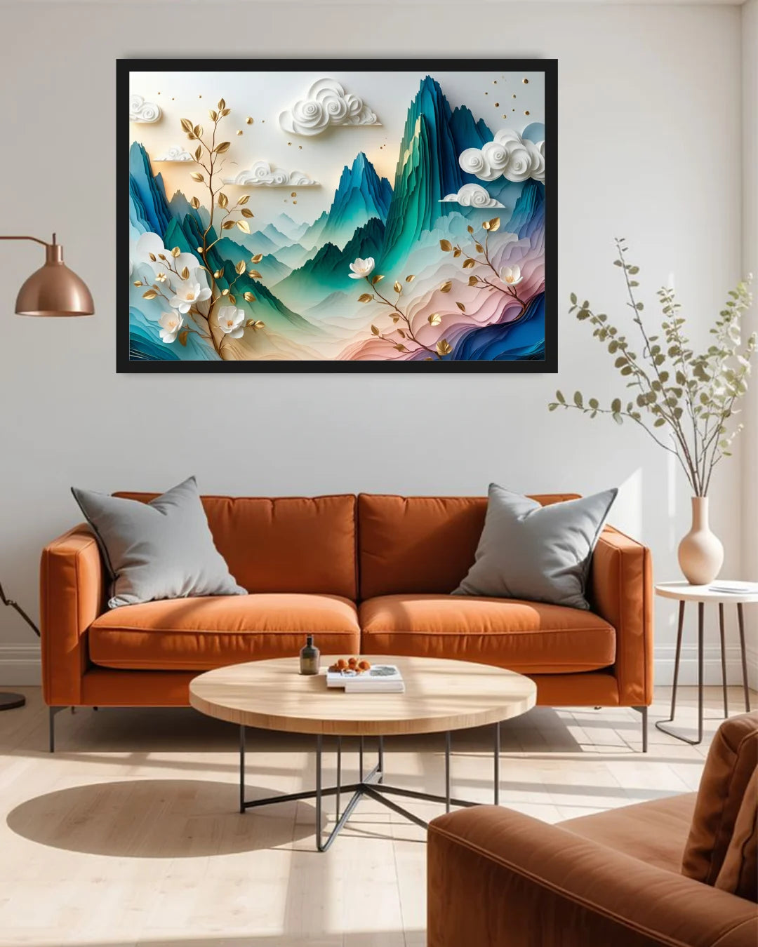 A framed abstract landscape wall art print hangs above a rust-orange sofa in a modern living room. The artwork features layered blue and teal mountains, white clouds, and soft pink and gold floral branches.