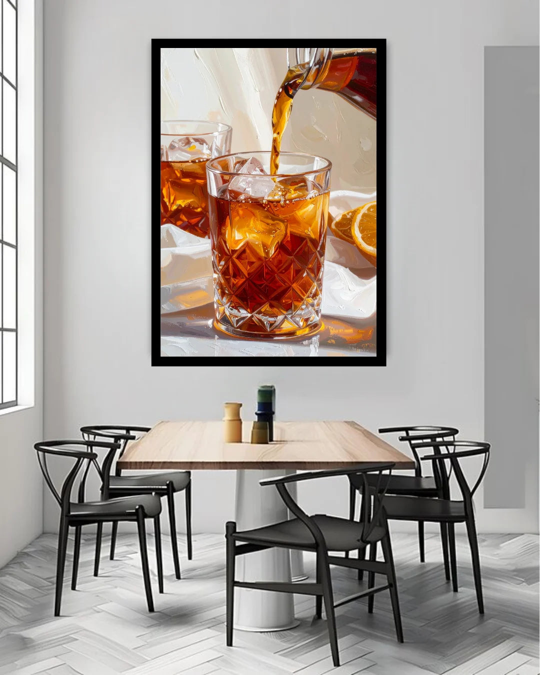 A framed wall art print depicting an amber drink being poured into a faceted glass, displayed above a dining table with chairs in a modern interior.