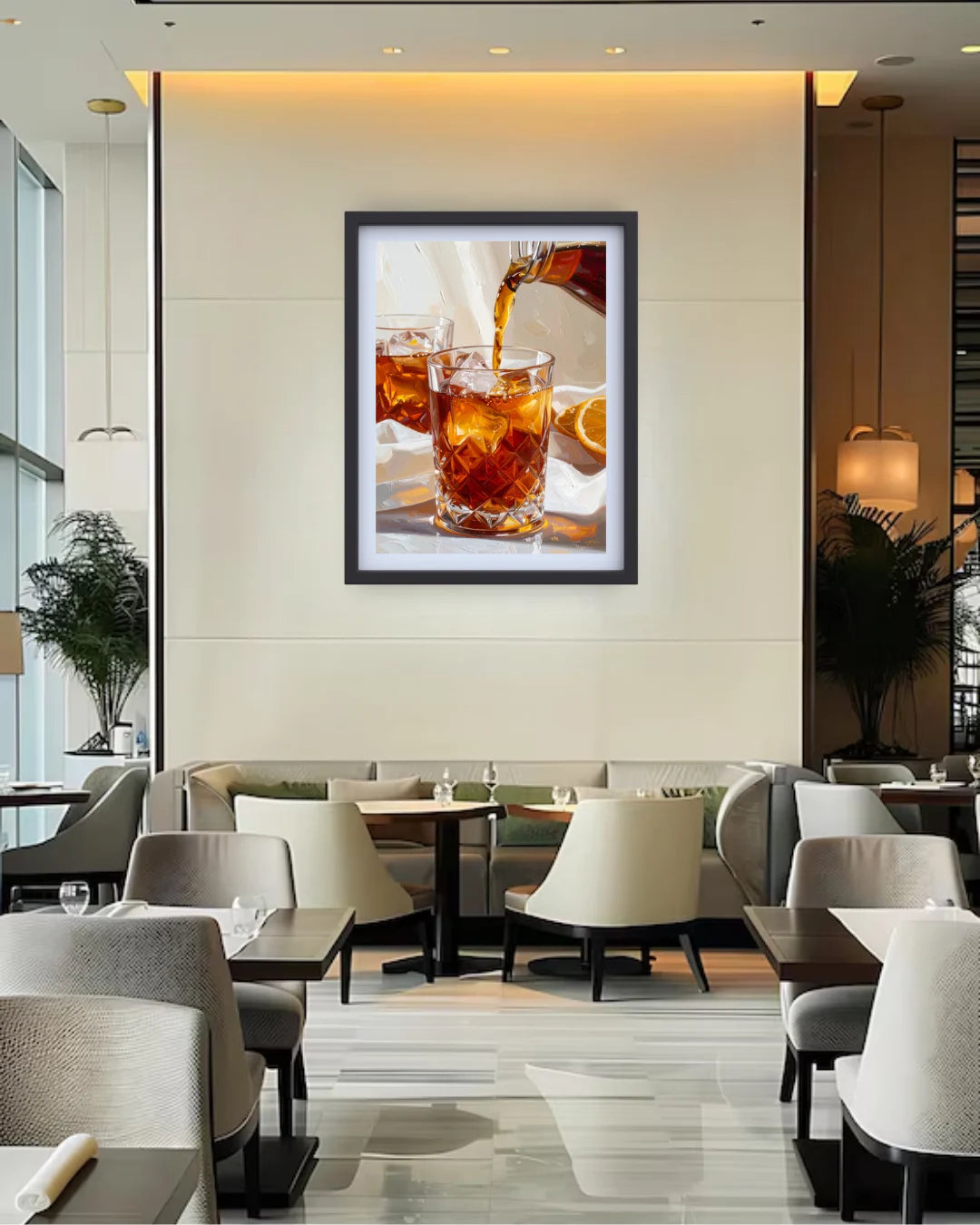 A framed wall art print depicting an iced drink with amber liquid and ice, displayed in a modern restaurant or lounge setting with tables, chairs, and warm ambient lighting.