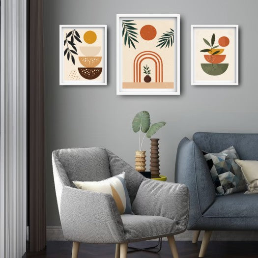 Three framed minimalist art prints with boho abstract designs in beige, orange, green, and brown, displayed on a gray wall above a gray armchair and blue sofa in a modern living room setting.