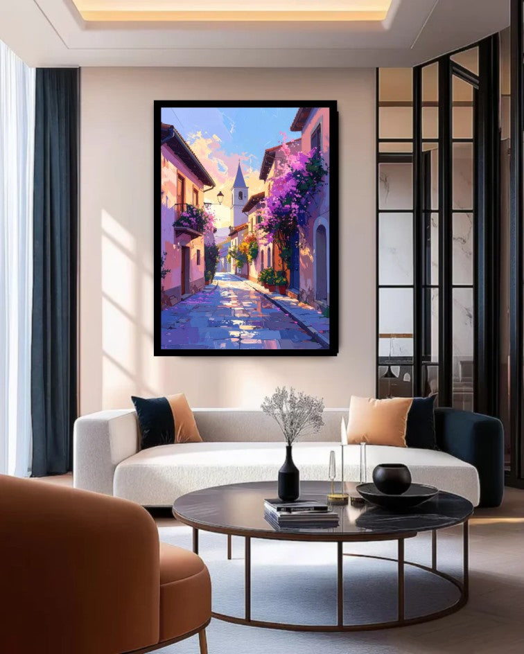 A framed vertical canvas painting of a colorful European street scene with purple flowers and a blue sky, displayed on a beige wall in a modern living room setting above a white sofa.
