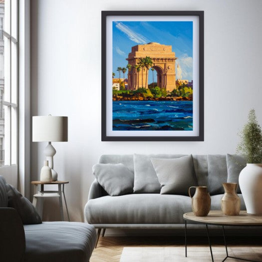 A framed vertical canvas print of the India Gate monument in Kolkata, painted in a vibrant impressionistic style, displayed on a white wall above a modern gray sofa in a styled living room.