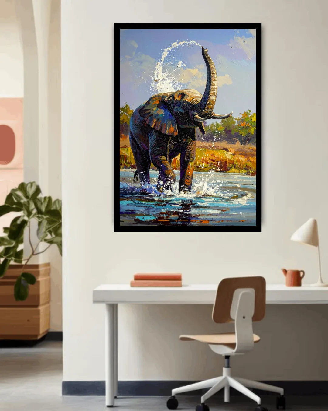 Framed painting of an elephant in a body of water on a wall above a desk.
