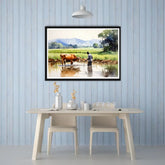 Framed landscape painting of a farmer and cow by a pond on a blue paneled wall above a dining table.