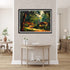 Framed landscape painting on a wall above a table in a room with wooden flooring.
