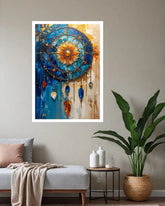 A framed abstract dreamcatcher wall art print hangs on a beige wall above a gray sofa in a styled living room. The artwork features a circular dreamcatcher design with blue, gold, and orange tones, and the room includes a plant, side table, and decorative bottles.