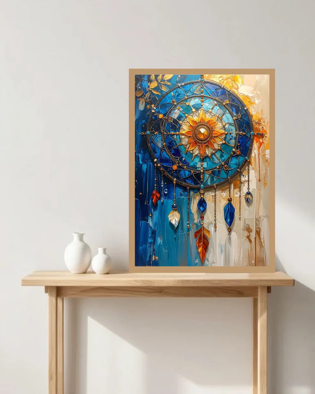 A framed abstract dreamcatcher-style wall art print leaning on a light wood console table against a white wall, with two small white vases beside it.