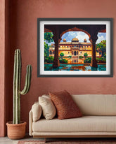 A framed art print depicting a colorful palace scene viewed through arches, displayed on a terracotta wall above a beige sofa with decorative pillows and a potted cactus nearby.