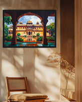 A framed painting of a traditional Indian palace courtyard with arches and a reflecting pool, displayed on a beige wall in a styled room with a wooden chair and dried flowers.