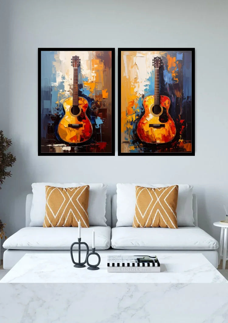 A pair of framed abstract paintings of acoustic guitars in warm orange, yellow, and blue tones, displayed side-by-side on a light gray wall above a white sofa with decorative pillows.