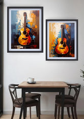 Two framed abstract paintings of acoustic guitars in warm orange, yellow, and blue tones, displayed on a white wall above a wooden dining table with two chairs.