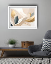 A framed abstract art print with flowing cream, beige, gold, and dark teal leaf-like shapes, displayed on a gray wall above a wooden console table in a modern living room setting.