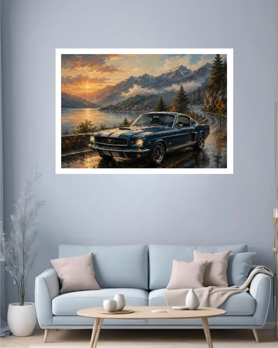 A framed landscape art print depicting a classic blue car on a winding road by a lake with mountains in the background, displayed on a light blue wall above a modern sofa in a living room setting.
