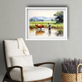 Framed landscape painting of a man and cow in a field with mountains, placed above a white armchair.