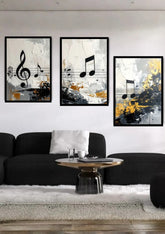 Three framed abstract musical note wall art prints hang above a black sofa in a modern living room setting. The prints feature black, white, gray, and gold/yellow abstract designs with musical notes.
