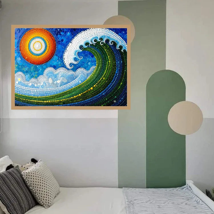 A framed abstract ocean wave painting with a bright sun, displayed on a bedroom wall above a bed with pillows. The artwork features a blue wave with green, yellow, and white details, and a multicolored sun in the upper left.