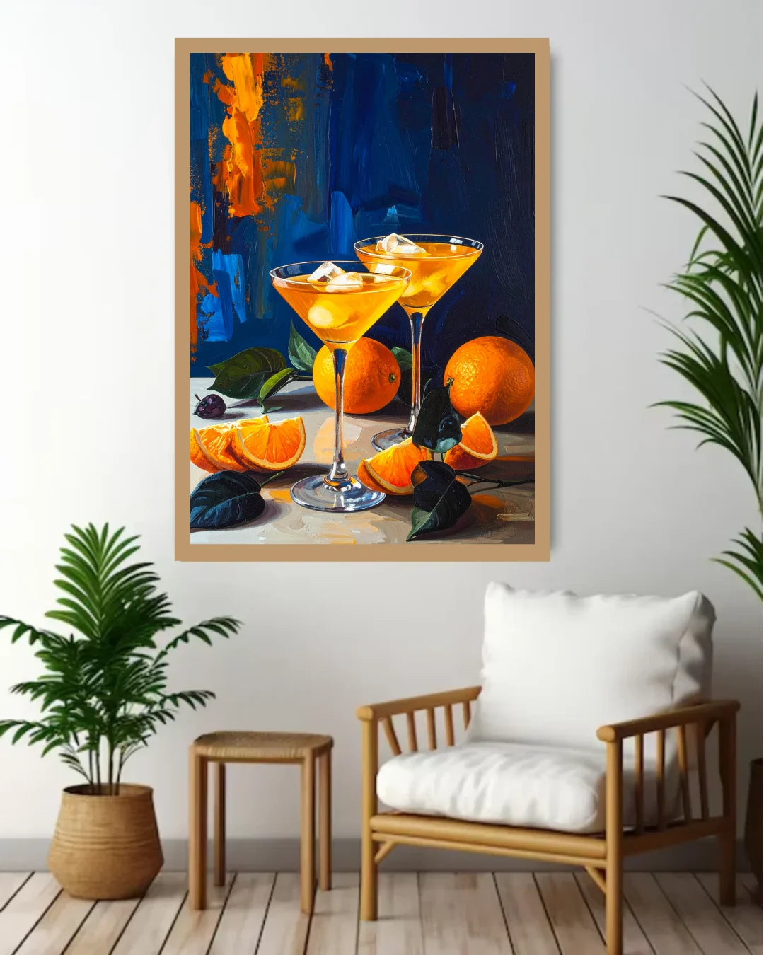A framed art print depicting a still life of orange cocktails and oranges, displayed on a white wall in a modern living room setting with a wooden chair, side table, and potted plants.