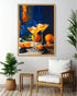 A framed art print depicting a still life of orange cocktails and oranges, displayed on a white wall in a modern living room setting with a wooden chair, side table, and potted plants.