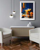 A framed art print depicting two orange cocktails and oranges on a dark blue background, displayed on a gray wall above a modern wooden console table in a styled living room setting.