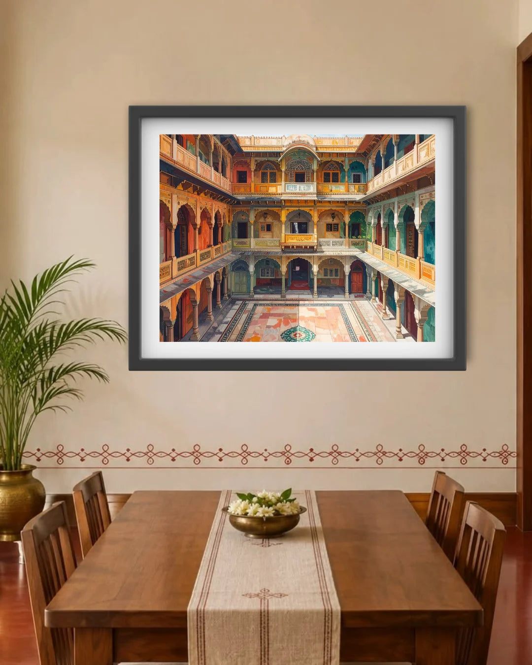 A framed art print depicting an ornate Indian courtyard with arches and balconies, displayed on a beige wall above a wooden dining table with chairs.