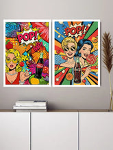 Two framed pop-art style wall prints with bold comic-style graphics and the word "POP!" displayed above a white cabinet against a light gray wall.
