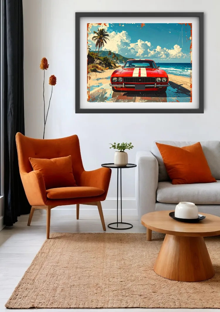 A framed art print depicting a red muscle car on a tropical beach, displayed on a white wall in a modern living room setting with an orange armchair, sofa, and wooden coffee table.