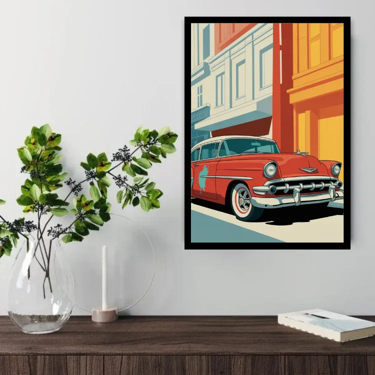 A framed pop-art print of a classic red car parked in front of colorful buildings, displayed on a light gray wall above a wooden console table with a glass vase of greenery, a candle, and a book.
