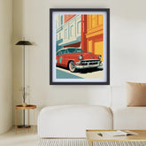 A framed pop-art style wall print showing a red vintage car parked in front of colorful buildings, displayed above a white sofa in a modern living room setting.