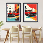 Two framed pop-art prints featuring red classic cars in stylized city street scenes, displayed side by side on a white wall above a wooden dining table and chairs.