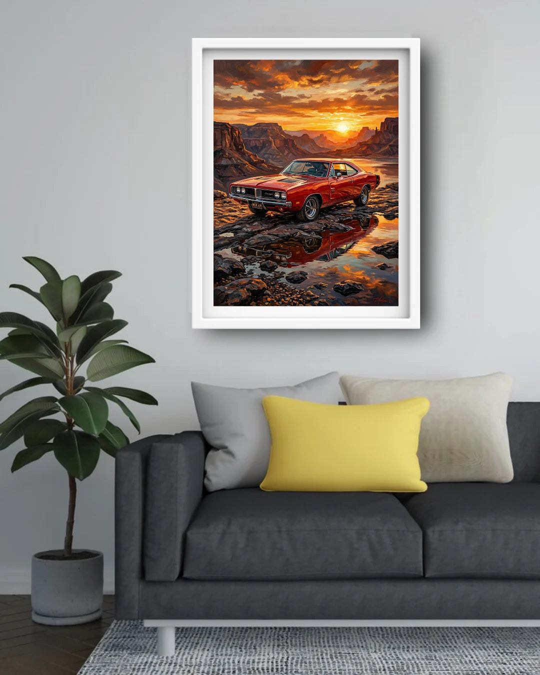 A framed art print of a red muscle car in a desert canyon at sunset, displayed on a light gray wall above a modern gray sofa with yellow and white pillows.