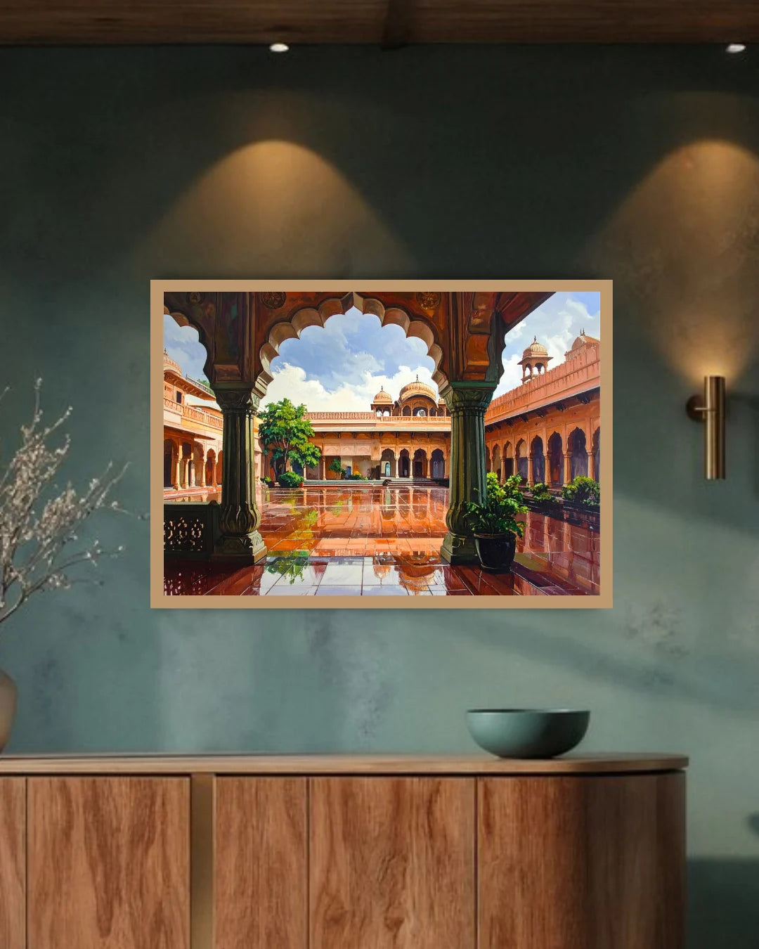 A framed painting of a traditional Indian courtyard with arches and a reflective pool, displayed on a textured teal wall above a wooden console table.