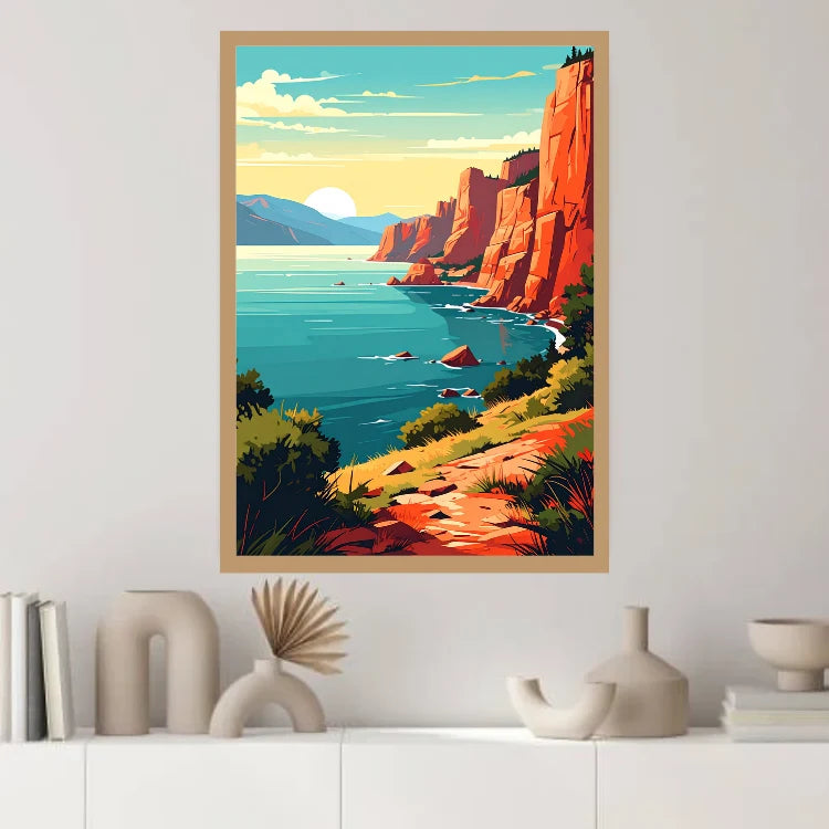 A framed art print featuring a retro-style coastal landscape with red rock cliffs, blue water, and a warm yellow sun, displayed on a white wall above a shelf with decorative objects.