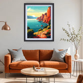 A framed vertical art print depicting a vibrant coastal canyon landscape with red cliffs, turquoise water, and a bright sun, displayed on a light gray wall above an orange-brown sofa in a modern living room setting.