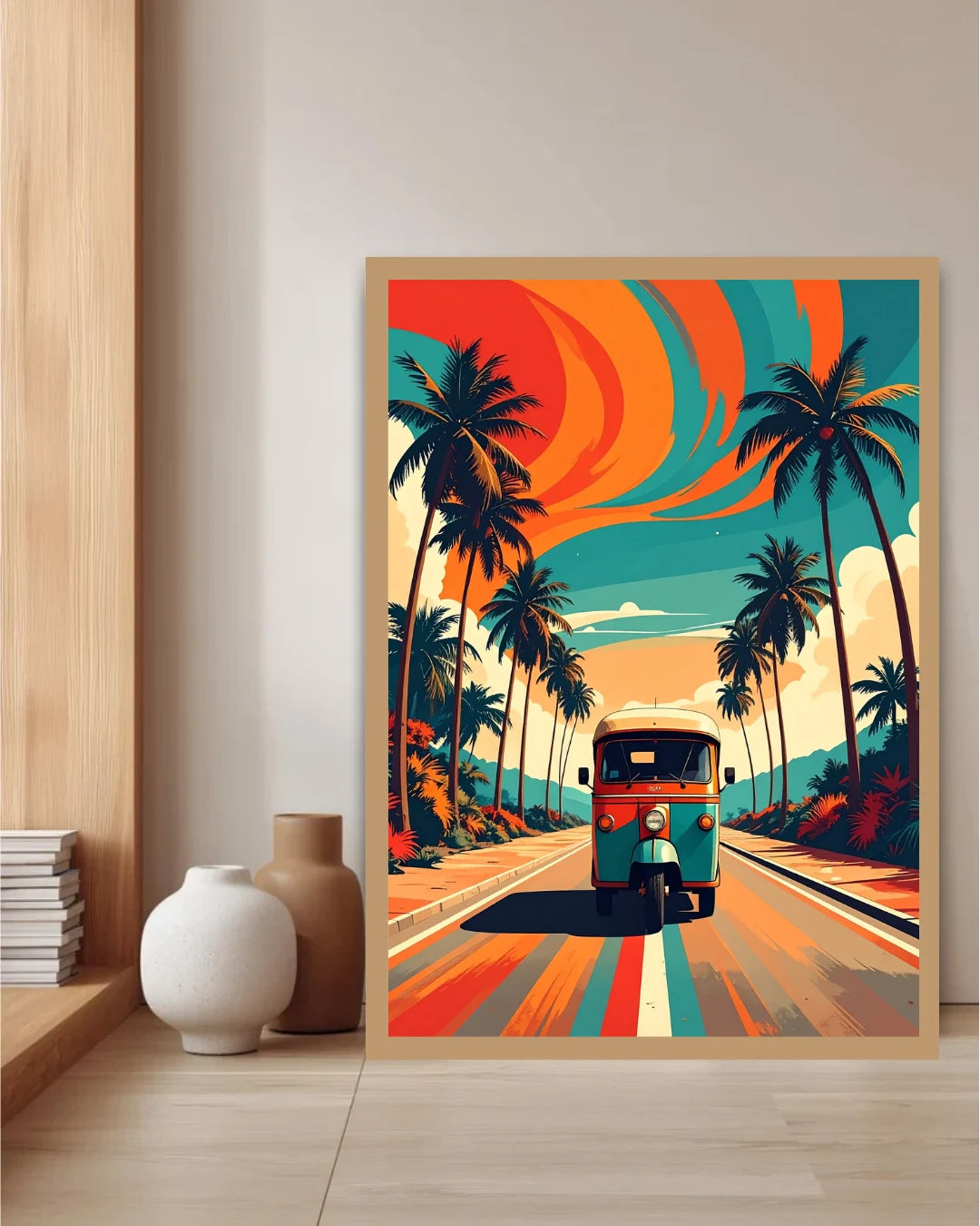 A framed art print leaning against a wall on a light wood floor, showing a retro-style tropical road scene with palm trees, a teal and orange vehicle, and bold swirling sky colors. The print is styled in a room setting with a wooden shelf, books, and two ceramic vases.