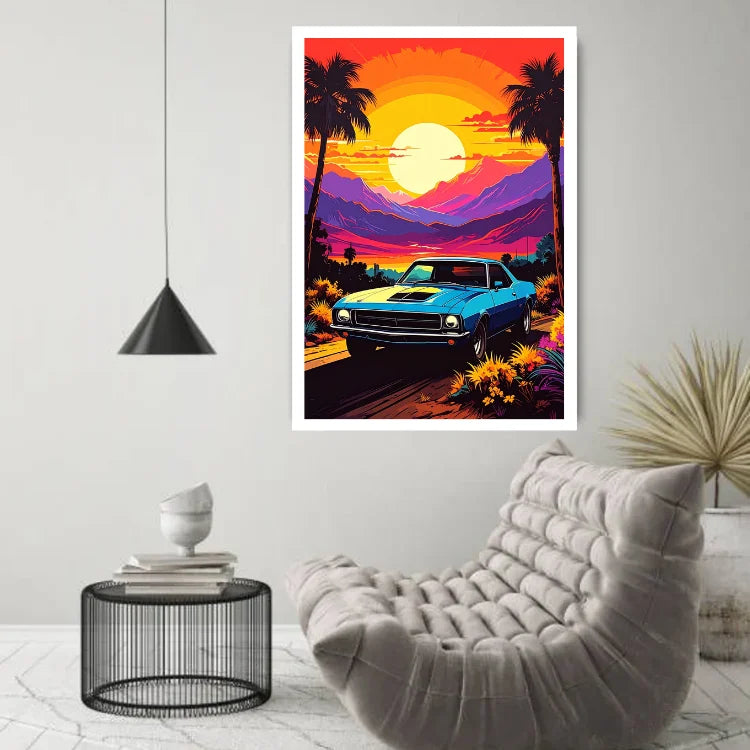 A framed wall art print featuring a retro blue muscle car on a sunset road with palm trees and mountains, displayed in a modern living room above a tufted chair and beside a small side table.