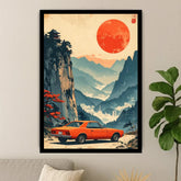 A framed art print featuring a retro orange car parked in a scenic mountain landscape with a large red sun, displayed on a light gray wall above a sofa with a potted plant nearby.