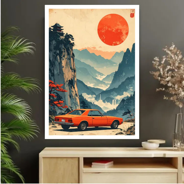 A framed vertical art print featuring a retro orange sports car parked in a misty mountain landscape under a large red sun, displayed on a dark wall above a light wood console table with decorative plants and bowls.