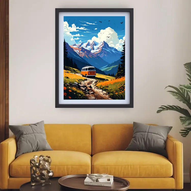 A framed art print depicting a scenic mountain landscape with a retro bus on a winding road, displayed on a beige wall above a yellow sofa in a living room setting.