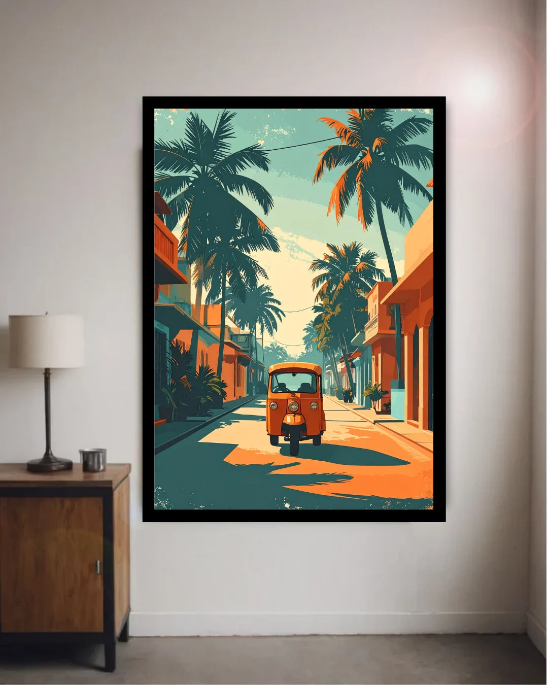 A framed art print depicting a retro orange auto-rickshaw on a tropical street lined with palm trees, displayed on a light gray wall in a modern room setting next to a lamp.