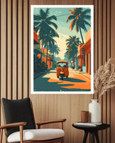 A framed retro-style art print featuring a teal tuk-tuk driving down a palm-tree-lined street, displayed on a wood-paneled wall above a chair and side table.