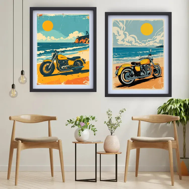 Two framed art prints featuring retro beach motorcycle illustrations hang on a light gray wall above two wooden chairs and small side tables in a styled interior room.